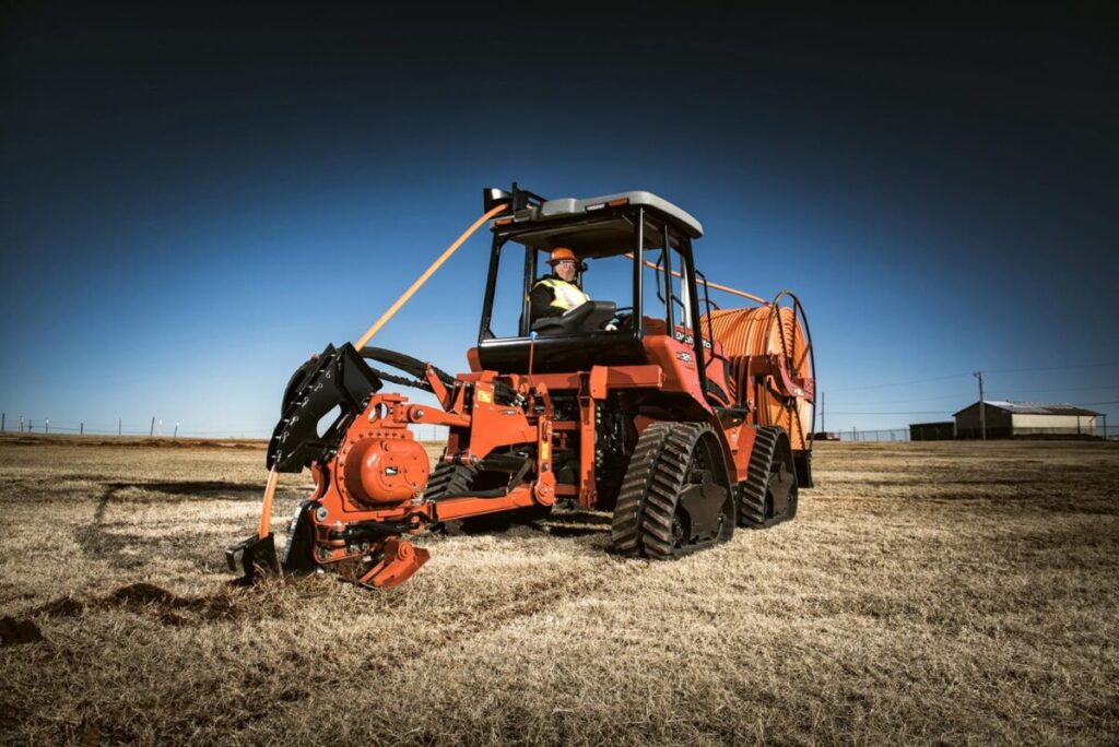Orange utility construction tractor equipped with rear attachment for underground field work