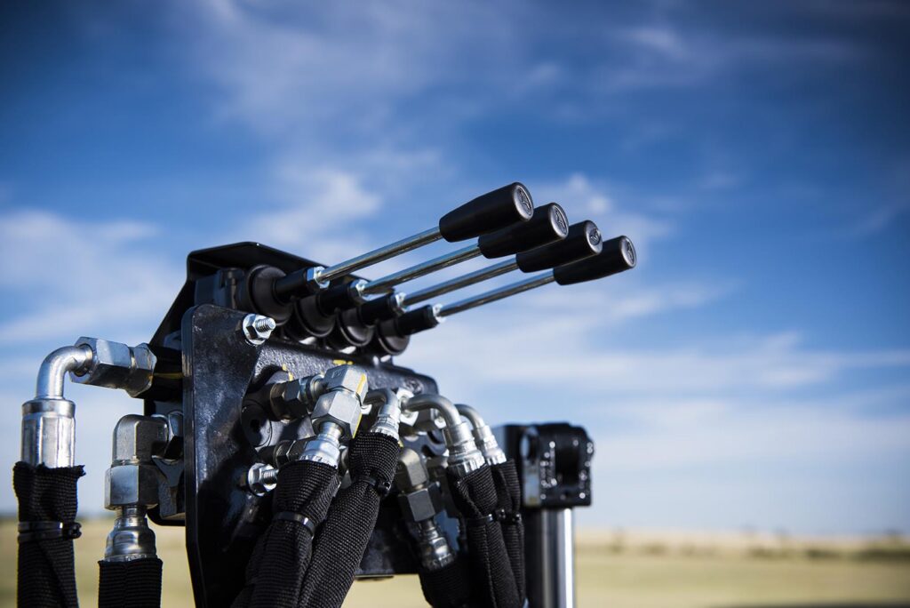 Close-up of Ditch Witch JT10 hydraulic control levers, hoses, and valve assembly against a blue sky